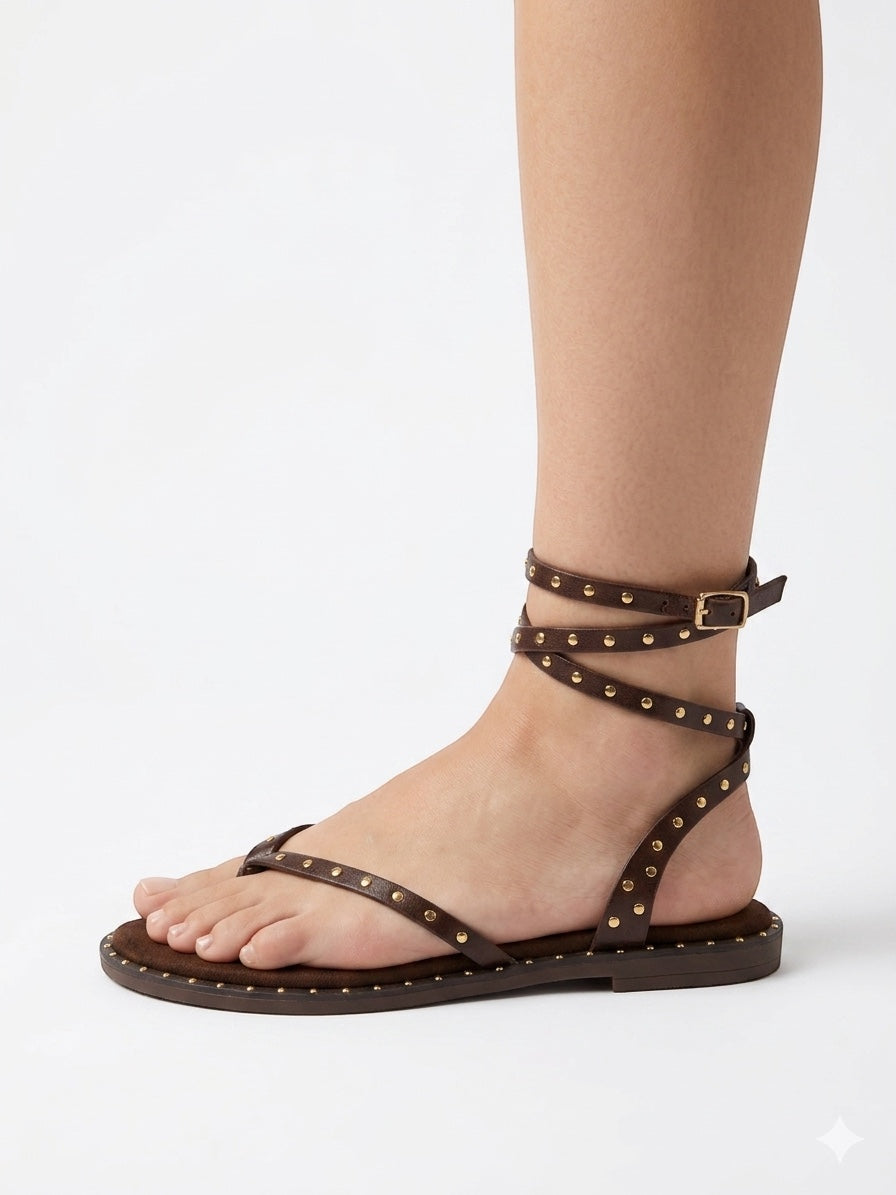 JESSICA brown leather Roman sandals with gold stud detailing and ankle strap. Flat sole, thong toe.